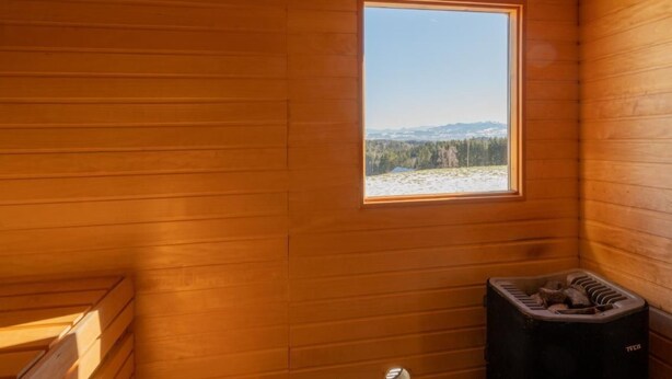 Interior de una cabaña de madera con ventana que muestra un paisaje nevado y una sauna.