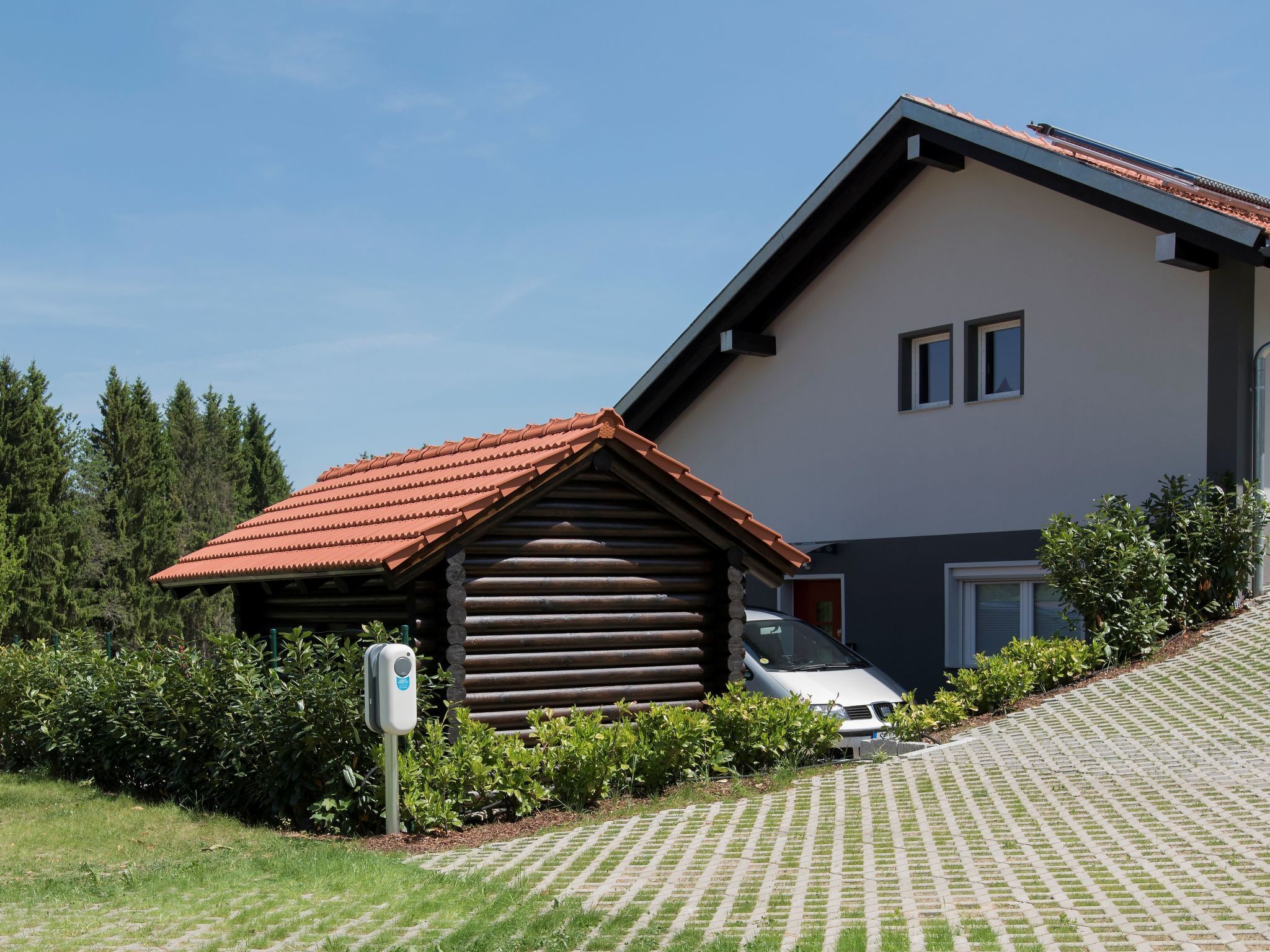 A modern house with a sloped roof, a log cabin extension, and a paved driveway.