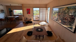 Un interior moderno con piso de madera, asientos de tatami, una zona de comedor y un ventanal con vistas al exterior.