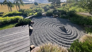 Un jardín con un sendero en espiral de grava, rodeado de diversas plantas y árboles.
