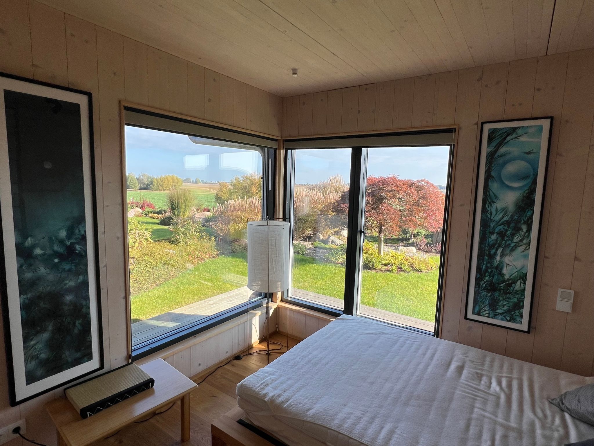 A bedroom with a large window, a bed, a bedside table, and a radiator.