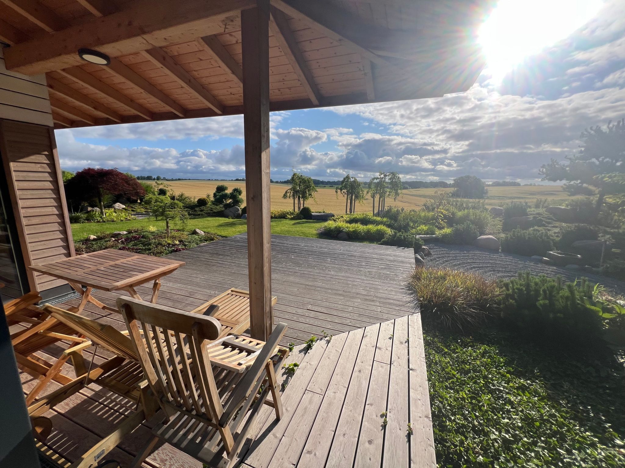 A wooden deck with a view of a rural landscape, including fields and trees.