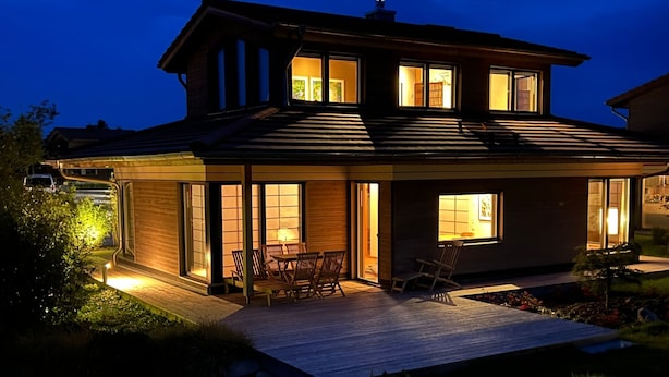 Una casa moderna de dos pisos con un patio, mobiliario exterior y ventanas amplias.