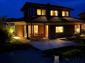 Ein modernes, zweigeschossiges Haus mit Terrasse, Sitzgelegenheiten im Freien und großen Fenstern.