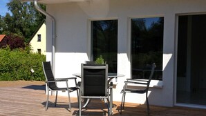 Eine Terrasse im Freien mit Tisch und vier Stühlen, einem kleinen Blumentopf und Blick auf ein Nachbarhaus.