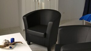 Ein Zimmer mit einem weißen Schrank, einem schwarzen Sessel, einem kleinen Tisch mit einer Kerze und zwei gerahmten Bildern an der Wand.