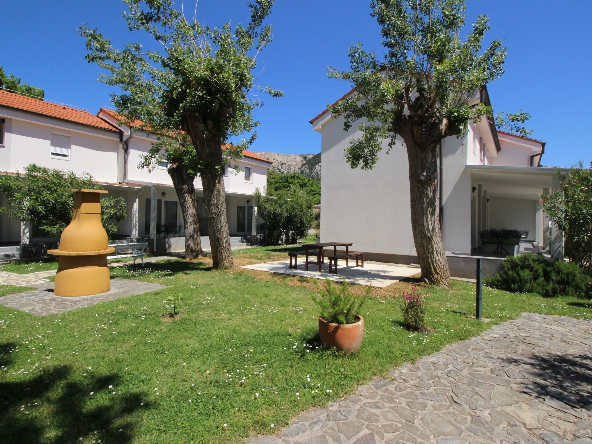 A courtyard with a large terracotta pot, a stone pathway, and a building with a tiled roof.
