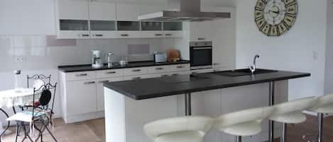 Una cocina moderna con armarios blancos, una isla central con taburetes y un horno empotrado, además de un reloj de pared.