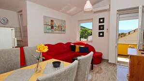 A modern living room with a red sofa, a dining table with chairs, a vase with flowers, and a painting on the wall. - Apartment Brnic8 by Interhome (Krk/Baška)