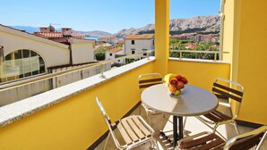 A balcony with yellow walls, a round table, and two chairs. There is a bowl of fruit on the table. - Apartment Brnic8 by Interhome (Krk/Baška)