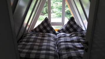 Ein schmaler, dreieckiger Raum mit einem Fenster am Ende, ausgestattet mit einem Bett mit kariertem Bettzeug und zwei Kissen.