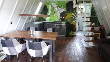 Eine kompakte Küche mit Essbereich, ausgestattet mit einem Holztisch und Stühlen, einer grünen Wandmalerei und einer Treppe zu einer oberen Ebene.