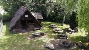 A rustic cabin with a sloped roof, surrounded by picnic tables and a fire pit.