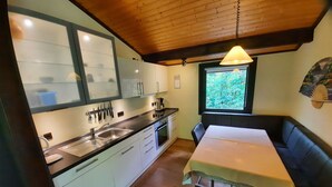 A compact kitchen with a dining area, wooden ceiling, and a window with a view of greenery.