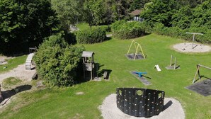 An aerial view of a playground with various play structures, surrounded by green grass and trees.