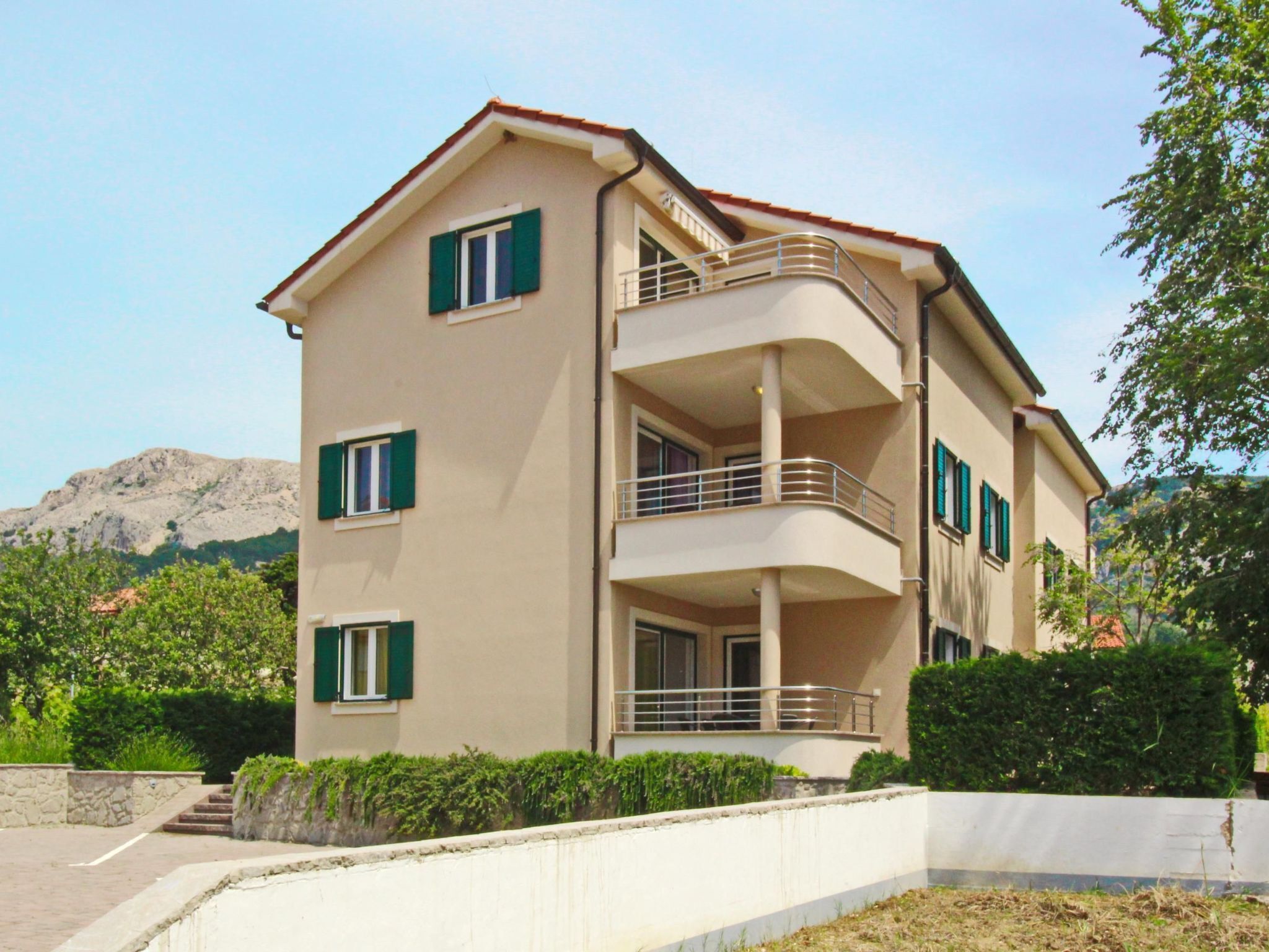 A multi-story building with balconies, a stone base, and a mountainous backdrop.
