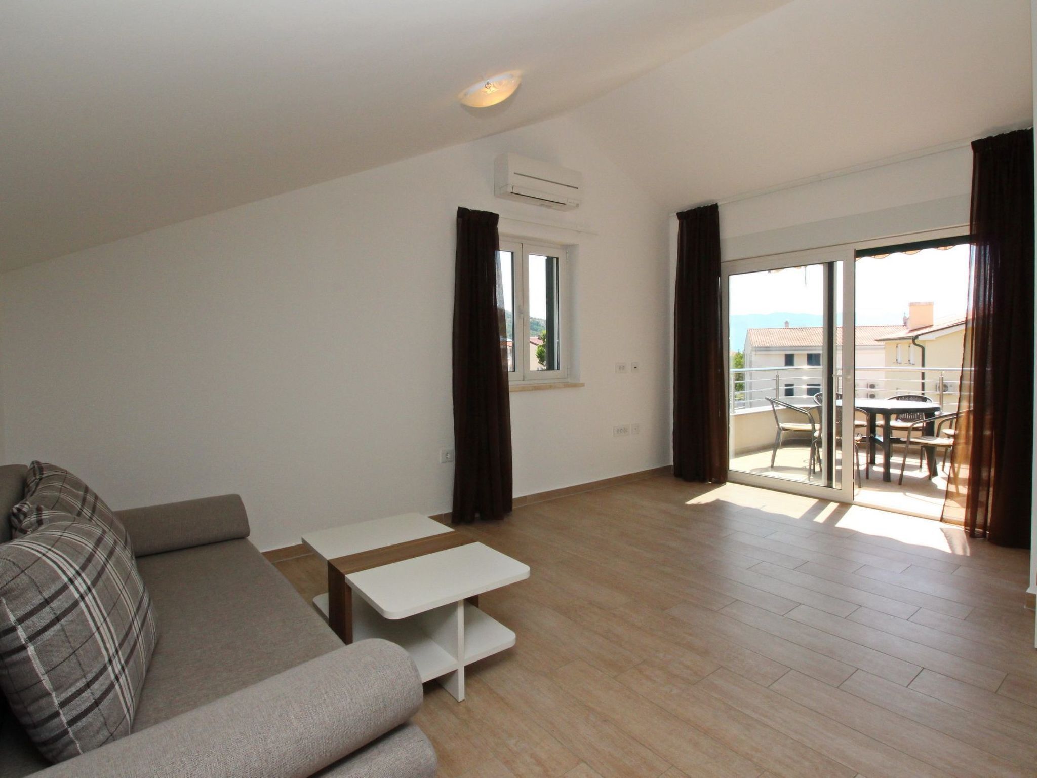 A modern apartment with a sofa, a small table, and a balcony with a table and chairs.