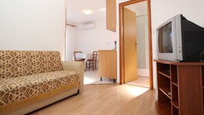 A living room with a sofa, a television on a wooden stand, and a dining area with chairs and a table. - Appartement in Baška mit Eigenem Balkon by Interhome (Krk/Baška)