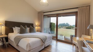 Ein geräumiges Schlafzimmer mit einem großen Bett, einem Schreibtisch und Blick auf einen Garten durch eine Glasschiebetür.