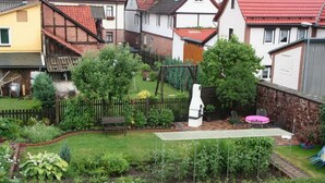 A residential backyard with a wooden fence, a swing set, a barbecue grill, and a small patio area with a table and chairs. - Gästehaus Tröbs by Interhome (Ilfeld)
