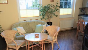 Uma sala de estar acolhedora com um sofá, duas poltronas de vime, uma mesa redonda e um vaso com planta.