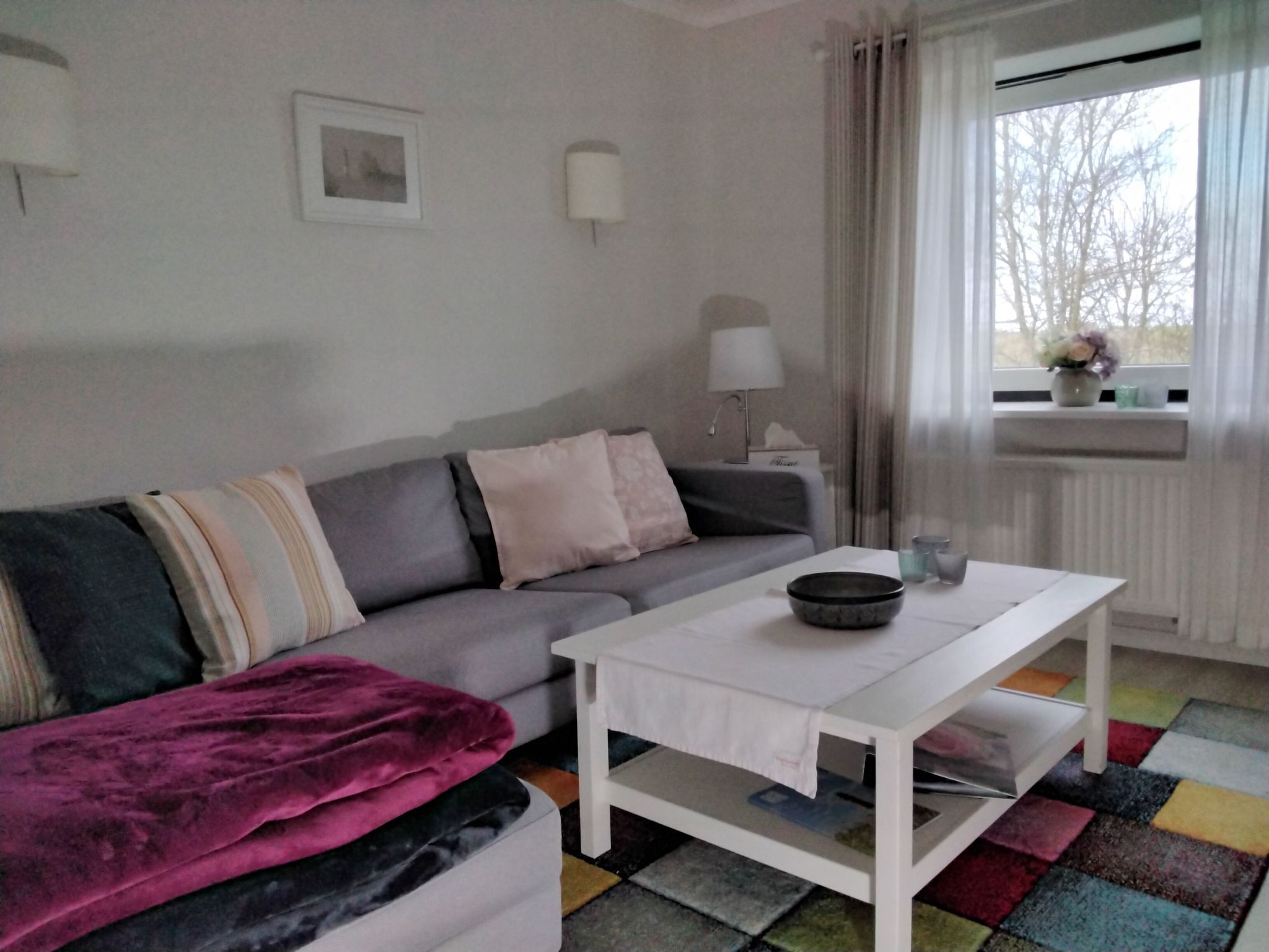 Un salon moderne avec un canapé gris, une table basse blanche et un tapis coloré.