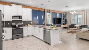 A modern kitchen with white cabinets, a microwave, stove, and dishwasher. There is a dining area with a sofa and coffee table. - Large 7BR getaway near Disney w/ pool (Kissimmee)