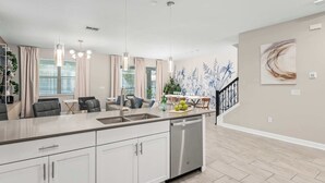 A modern kitchen with a dishwasher, pendant lights, a dining area with a table and chairs, and a staircase. - Large 7BR getaway near Disney w/ pool (Kissimmee)