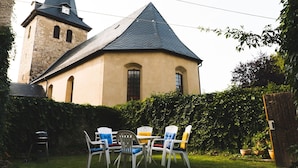 A church with a steeply pitched roof and a bell tower, surrounded by a well-maintained garden with a table and chairs. - Gemütliche Ferienwohnung für die ganze Familie by Interhome (Ballenstedt)