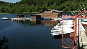 A lakeside dock with boats, wooden buildings, and a forested hill in the background. - Gemütliche Ferienwohnung für die ganze Familie by Interhome (Ballenstedt)