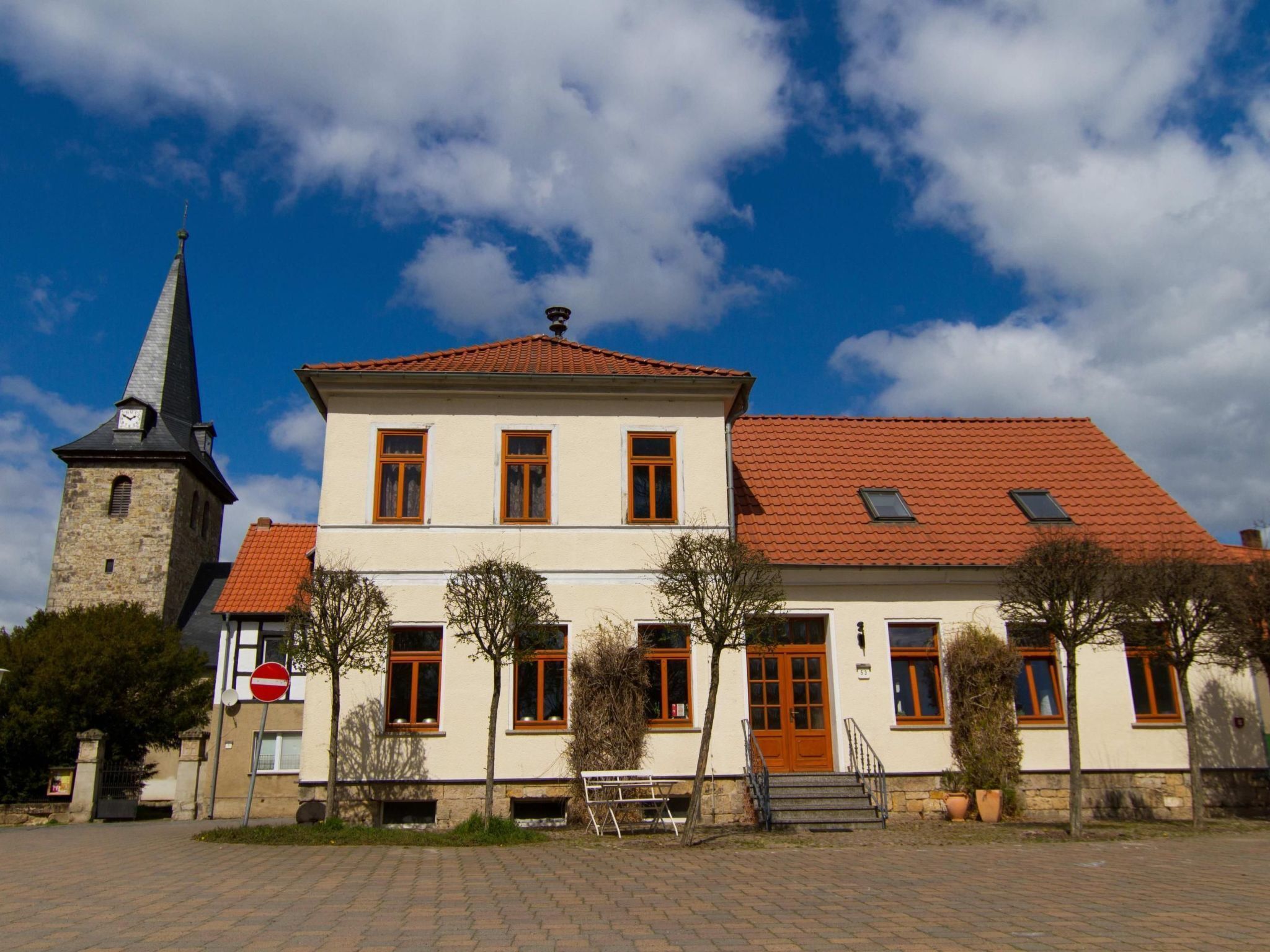 Een gebouw met twee verdiepingen, een rode pannendak en een kerktoren aan de linkerkant.