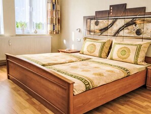 A double bed with a wooden frame and a patterned bedspread, a bedside table with a lamp, and a wall with a decorative piece. - Fewo 4 Schneider · Südstadt · Parkplatz · WLAN by Interhome (Görlitz)