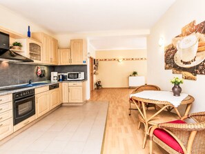 A modern kitchen with a built-in oven, microwave, and coffee maker. There is a dining area with a wicker table and chairs. - Fewo 4 Schneider · Südstadt · Parkplatz · WLAN by Interhome (Görlitz)