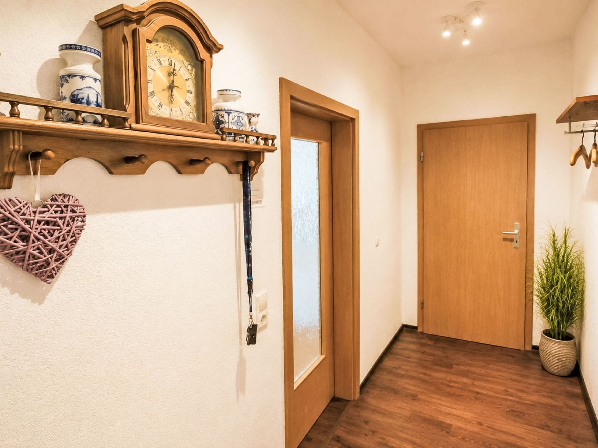 A hallway with a wooden door, a wall-mounted clock, and a decorative heart-shaped item.