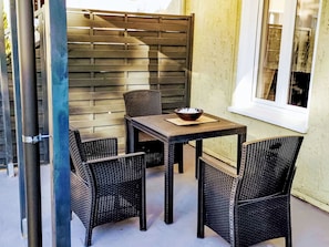 Un espace extérieur aménagé avec une table et quatre chaises, une cloison en bois et une fenêtre donnant sur un paysage agréable.