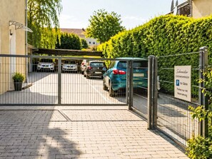 Un parking clos, avec plusieurs voitures stationnées, un panneau indiquant des places de stationnement réservées, et un bâtiment à l’architecture moderne en arrière-plan.