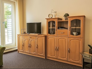 Un salon avec un téléviseur posé sur un meuble en bois, une table basse en verre et une vue par la fenêtre.
