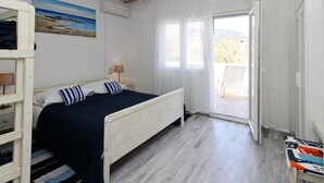 A bedroom with a bed, a nightstand, a lamp, a painting, and a view of the outdoors. - Fantov Zarok A4 br.3 by Interhome (Krk/Baška)