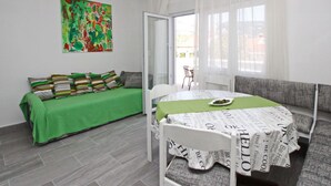 A modern bedroom with a green sofa, a white bed with a newspaper print bedspread, and a colorful abstract painting on the wall. - Fantov Zarok A4 br.3 by Interhome (Krk/Baška)