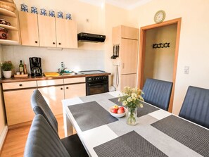 A compact kitchen with a dining area, including a table with placemats, a bowl of fruit, and a vase of flowers. - Fewo 2 Schneider – Südstadt · Dachterrasse WLAN by Interhome (Görlitz)