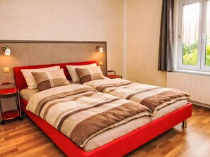 A double bed with a red frame and striped bedding, two bedside tables with lamps, a window with curtains, and a radiator. - Fewo 2 Schneider – Südstadt · Dachterrasse WLAN by Interhome (Görlitz)