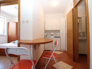 A compact kitchen with a dining area, a bed, and a bathroom visible through an open door. - Wohnung in Baška by Interhome (Krk/Baška)