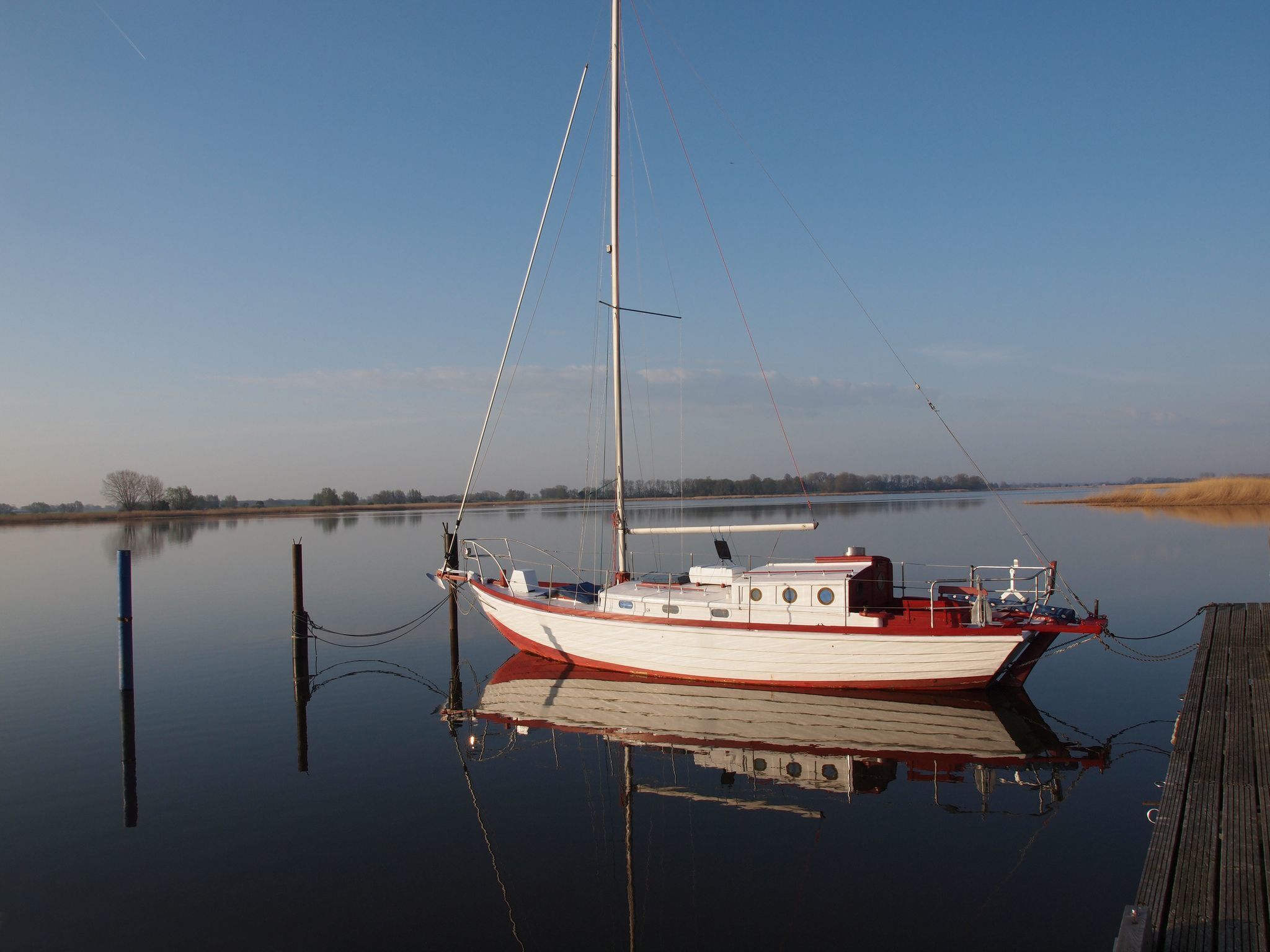 A boat docked at a calm river with a wooden pier.