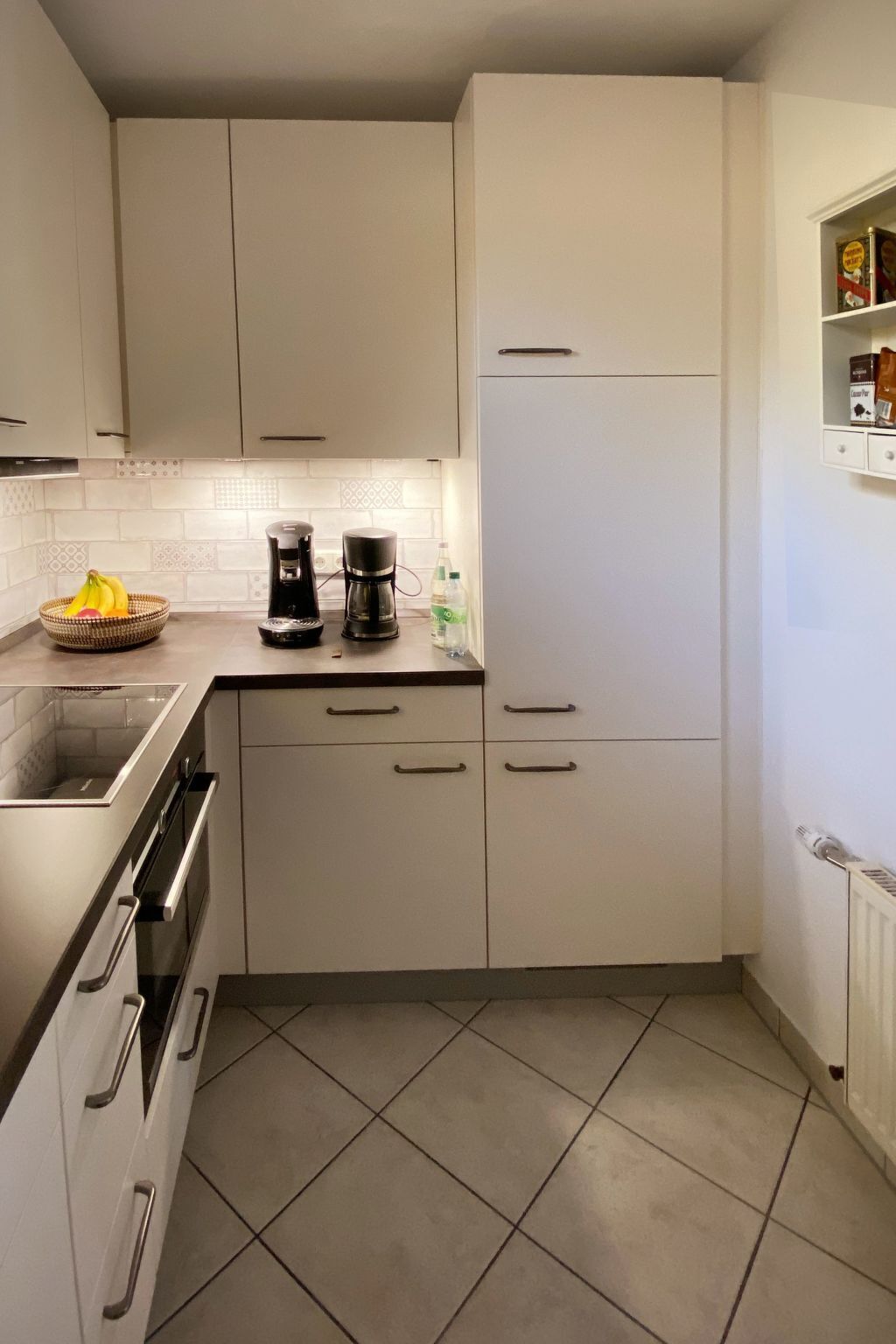 Une cuisine avec des meubles blancs, une machine à café et un panier de fruits.