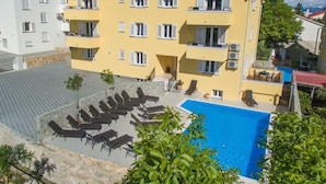 A multi-story building with a swimming pool, outdoor seating, and a red-tiled roof. - Gorica II A2+2 br.2 by Interhome (Krk/Baška)