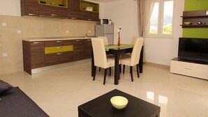 A modern kitchen with wooden cabinets, a dining table with chairs, a flat-screen TV, and a small table with a bowl. - Gorica II A2+2 br.2 by Interhome (Krk/Baška)