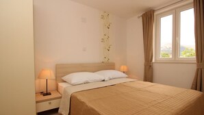 A bedroom with a bed, two bedside lamps, a nightstand, a window with curtains, and a wall decoration. - Gorica II A2+2 br.2 by Interhome (Krk/Baška)
