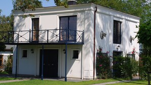 Un edificio bianco a due piani con un balcone, un'entrata e un piccolo giardino con fiori rosa.