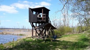 A wooden observation tower with a platform and a covered upper area, situated by a body of water with a bicycle parked nearby. - Ferienhaus Claire am Klostersee Urlaub mit Hund by Interhome (Dargun)