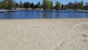 A sandy beach with a calm water body, trees, and a distant building. - Ferienhaus Claire am Klostersee Urlaub mit Hund by Interhome (Dargun)